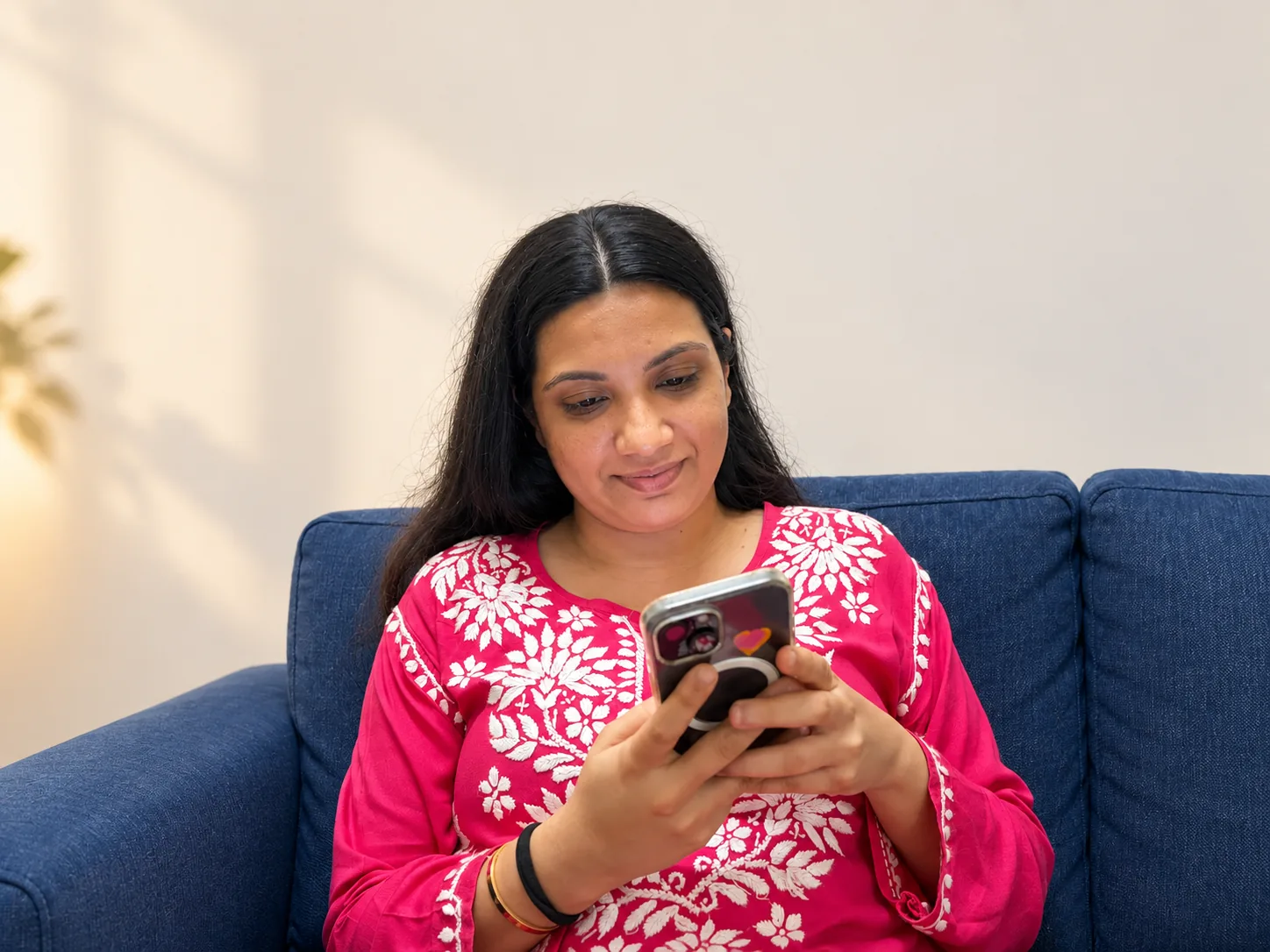 A customer smiling at her phone while seated on a sofa
